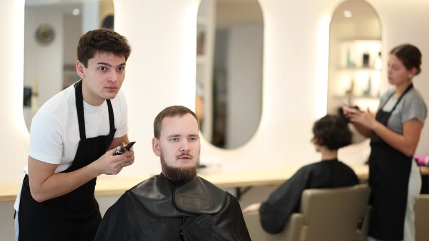 Young guy hairdresser stylist gives haircut to young male client in beauty salon. High quality 4k footage