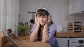 Asian girl wearing headphones and softly nodding her head to the beat. Adorable young little kid feeling happy and enjoying her favorite music while spending a peaceful holiday in the kitchen at home. - Powered by Shutterstock - Get 15% off with code: PIKWIZARD15