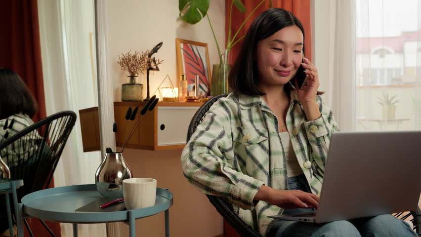 Happy Asian Korean woman talking mobile phone smartphone working typing laptop computer female entrepreneur manager call businesswoman smiling girl office home indoors consulting business freelancer