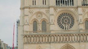 Close upshot of the facade of Notre-Dame Cathedral in Paris, showcasing rose window, rows of stone saints, arched stained-glass windows, Gothic arches, and restoration equipment - Powered by Shutterstock - Get 15% off with code: PIKWIZARD15