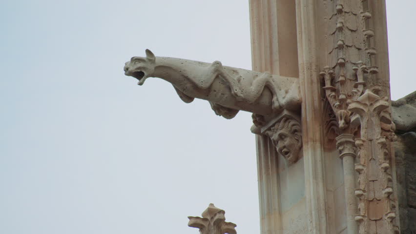 Close-up of a gothic gargoyles on Notre-Dame Cathedral, Paris, showing detailed stone carving of a mythical creature with a grotesque human face at its base, used for water drainage.