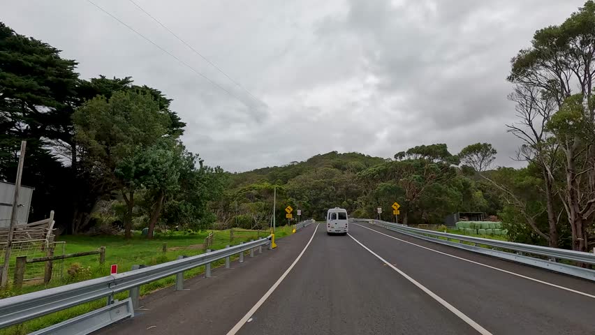 Forward-facing hyperlapse captures a winding drive on the Great Ocean Road, Victoria, Australia, through lush forests and open farmland under overcast skies