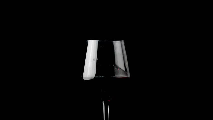 hand tilts a glass filled with rich red wine against a black backdrop, creating an intimate atmosphere perfect for relaxing. The evening is quiet and inviting.