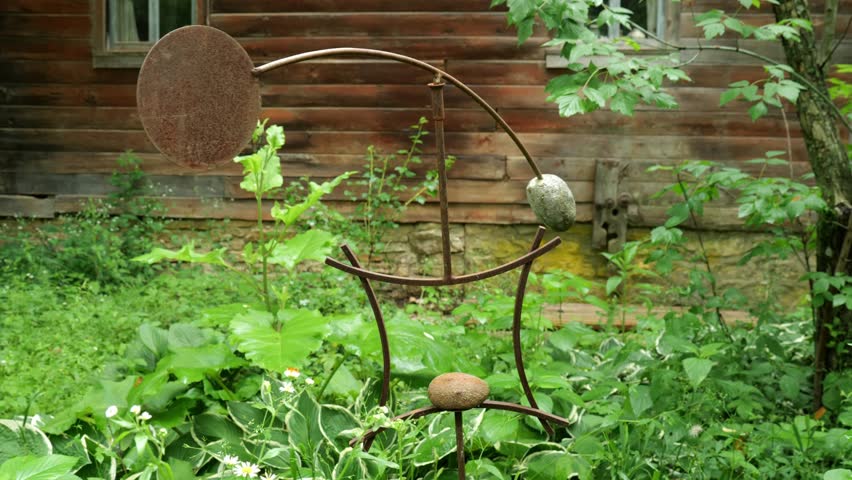 Kinetic Sculpture of Steel and Rock Swaying Gently in front of Cabin