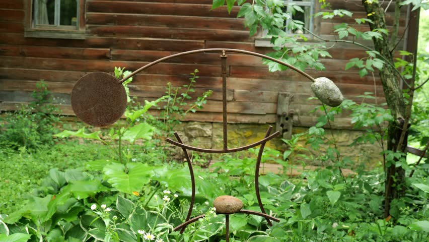 Kinetic Sculpture of Steel and Rock Rocking in front of Cabin