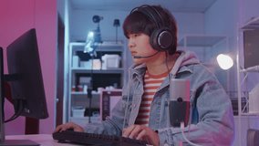 Young Asian gamer boy is excited playing online video games on gaming computer with keyboard and headset, cyber virtual technology, esports entertainment in dark room, fun teenage streaming lifestyle. - Powered by Shutterstock - Get 15% off with code: PIKWIZARD15