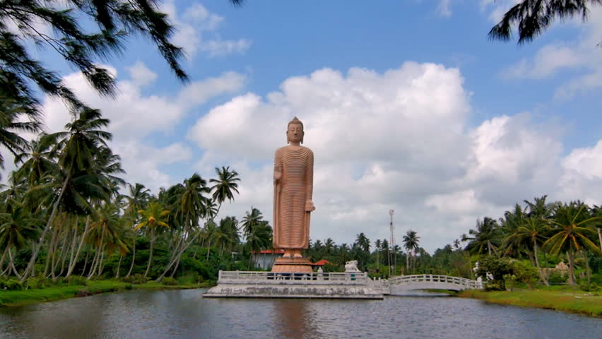 Distant view of giant Buddha statue framed by palm trees and lake water