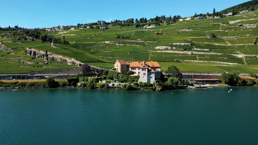 Parallax drone shot of Glerolles Castle, Lake Geneva and Lavaux terraced vineyards in the back during the day in Saint-Saphorin, canton of Vaud, Switzerland
