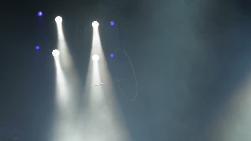 A circus hoop for the performance of aerialists hangs under the dome of the circus under the light of colorful spotlights and smoke. Circus equipment, background. A circus show.