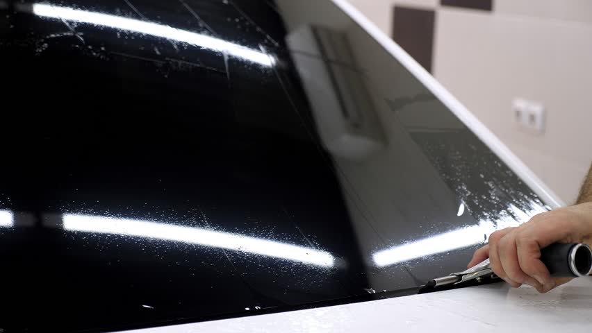 A close-up of the car servicemaster glues the tinting film on the glass, he smoothes the foil with a spatula. The process of tinting a car in a car service.