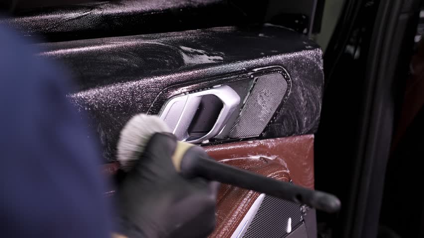 Cleaning the car interior with a brush. Auto detailing worker cleaning car interior, car detailing concept. Dust removal from the dashboard of the car with a brush.