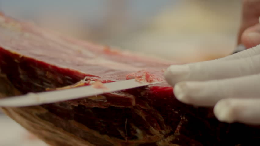 An detailed closeup of a whole leg of cured ham resting on a wooden board ready for slicing
