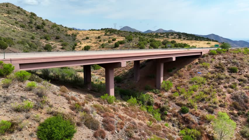 Aerial view of a concrete highway crossing a bridge, winding through a landscape of dry grassy hills and distant mountains, Pine, Arizona, United States.