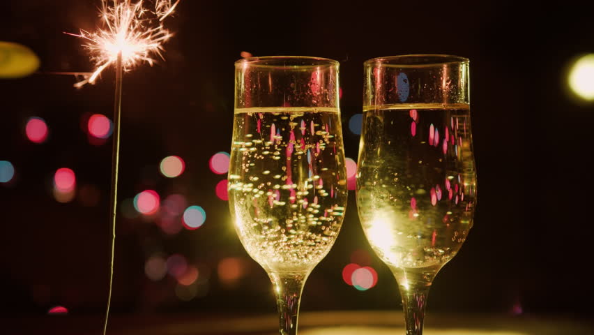 Two glasses of sparkling champagne and sparkler on festive background.