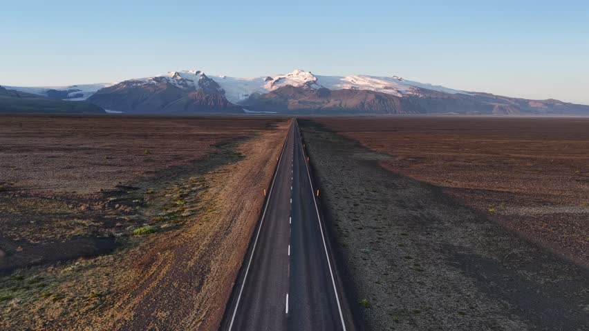 Aerial view of a long straight road cutting through a vast landscape leading towards snow-capped mountains, Iceland roads, Iceland.
