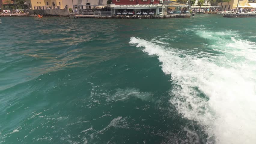 Speed boat leaving Lake Garda harbour, looking back POV to mountains