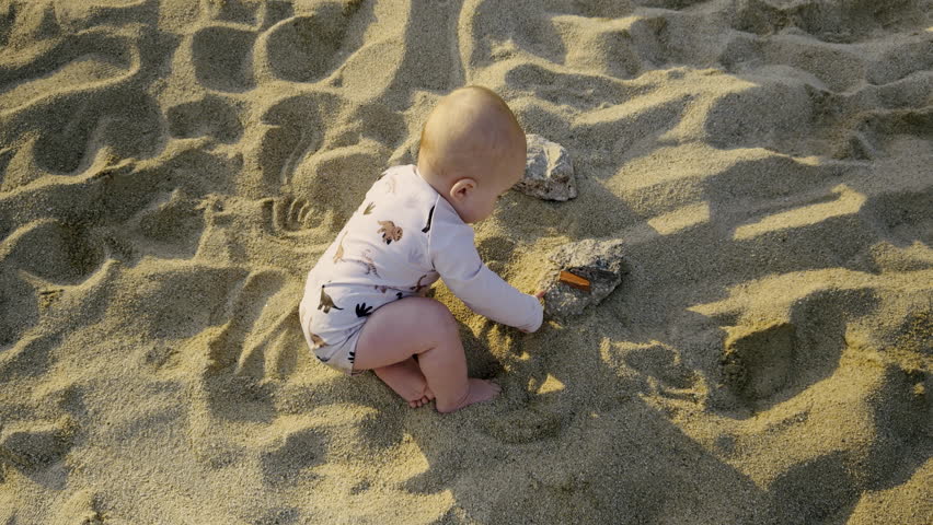 Young boy playing in soft sand on a sunny beach, exploring textures and shapes, surrounded by gentle waves and a bright blue sky, enjoying a carefree moment of childhood