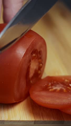 Vertical video. Girl cuts a ripe red tomato into slices with a knife on a wooden cutting board. Close-up. Cutting ripe vegetables for a vegetarian salad. Taking vitamins. Healthy food.