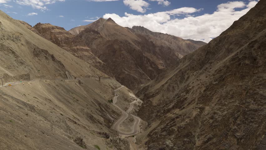 Main road from Kargil to Leh traffic on bendy road through rocky valley. Timelapse of cars and motorbikes winding through landscape looks like toys.