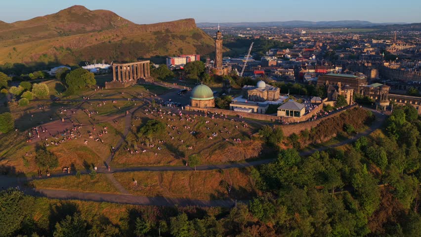 Aerial video of Calton Hill at Sunset with people socialising and Holyrood park hills on the background.