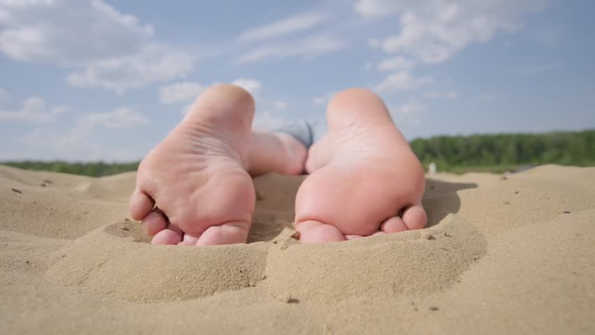 Woman legs barefoot relaxing lying on sandy beach on stomach, close up on feet