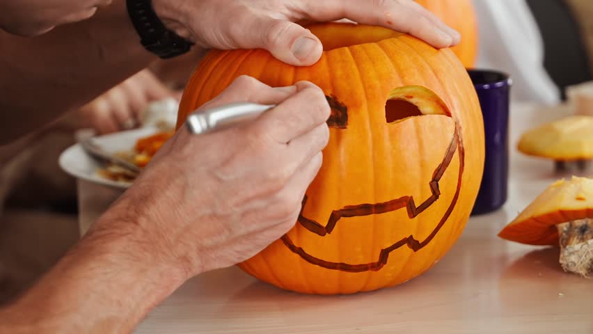 Person carving Halloween pumpkin along a hand-drawn sketch to cut spooky eyes and mouth, jack-o-lantern design