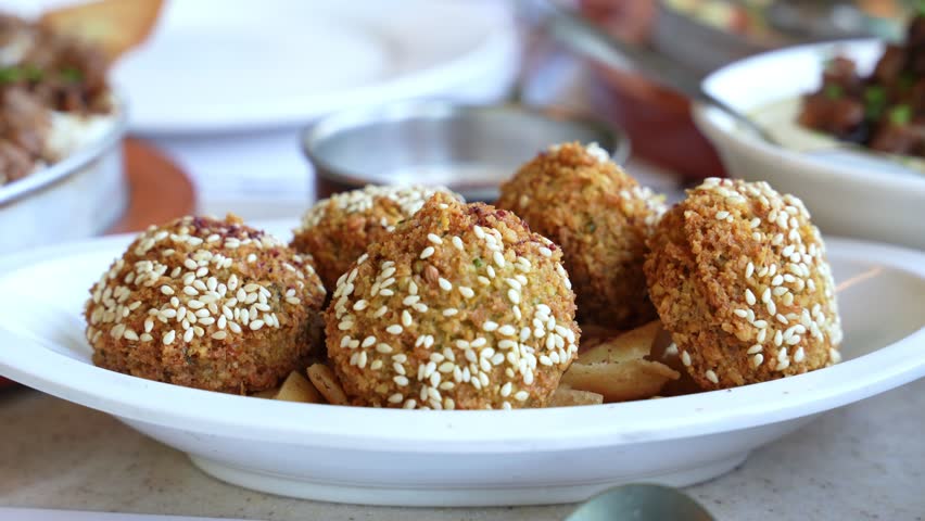 Appetizing close-up of golden falafel with sesame seeds served on a white plate, perfect for promoting Mediterranean, vegetarian, or healthy cuisine.