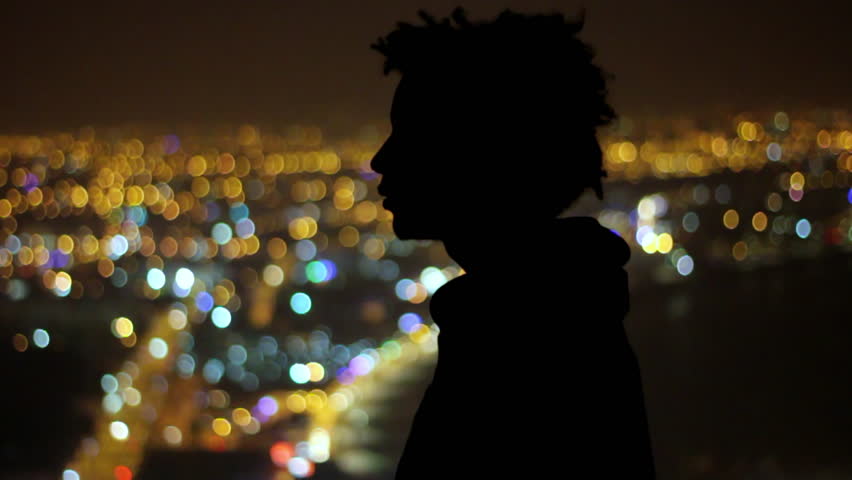 Silhouette of a young man gazing over vibrant city lights in the peaceful night
