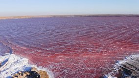 Low drone shot flying just above a vibrant pink salt lake in Namibia, with small waves rippling across the water. Walvis bay - Powered by Shutterstock - Get 15% off with code: PIKWIZARD15