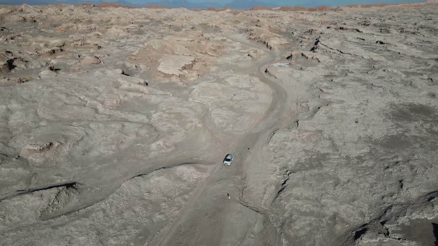 A drone view of White car driving through the rugged, arid terrain of Death Valley in the Atacama Desert, Chile