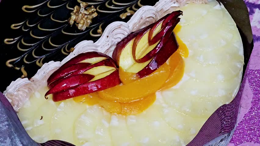 Round birthday cake of two halves different pieces sponge creamy cake for celebrations, dark chocolate topped with walnut, caramel, whipped vanilla cream, slices of pineapples, apples, peach, nuts