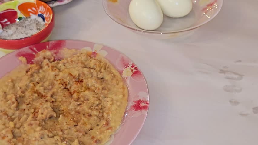 Egyptian breakfast of a plate of mashed fava beans mixed with oil, sesame tahini, cumin, spices, traditional popular street Egyptian fava bean, boiled eggs, flat bread, sliced tomatoes and salt