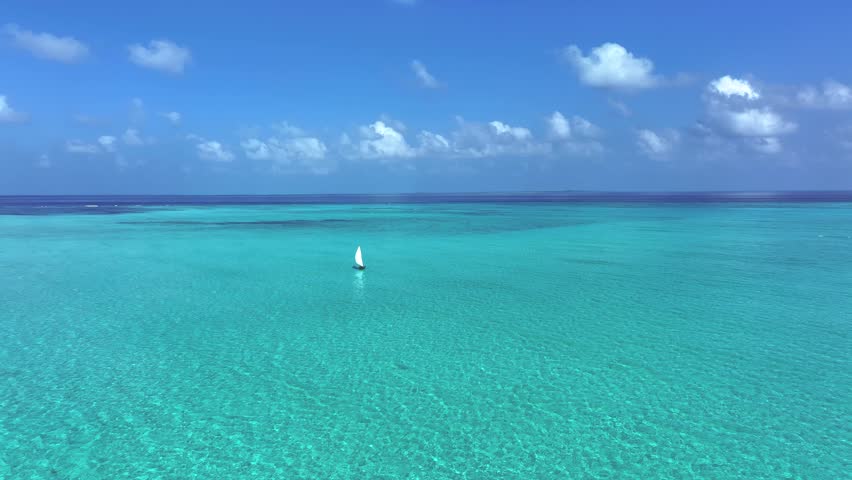 Aerial view of a lone sailboat sailing through the mesmerizing turquoise lagoon under a clear blue sky, Bileffahi, Shaviyani Atoll, Maldives.