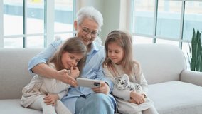 Happy family at home. Two little girls sisters twins grandmother enjoying time together watching video on phone. Good time at home. Grandma granddaughters child kids together. Family generations - Powered by Shutterstock - Get 15% off with code: PIKWIZARD15
