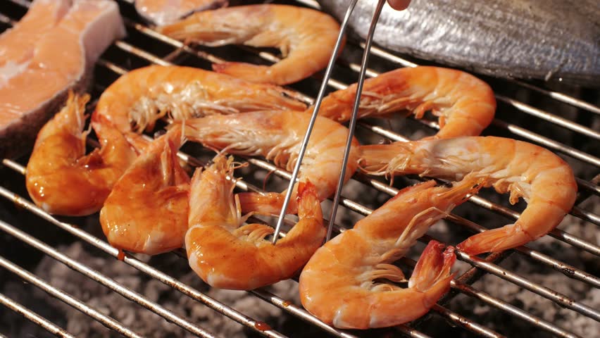 Chef cooking shrimps with oil and spices on grill close-up. Prawns on fire throwing them on pan. Dorado and salmon fish steak on frying grill. Restaurant Food concept. Sea food barbecue.