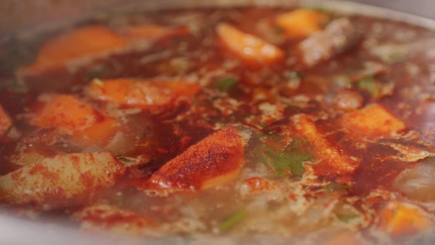 Hungarian goulash soup cooking close-up in pot, chef cook traditional polish or zech soup in restaurant. 