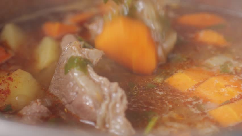 Hungarian goulash soup cooking close-up in pot, chef cook traditional polish or zech soup in restaurant. 
