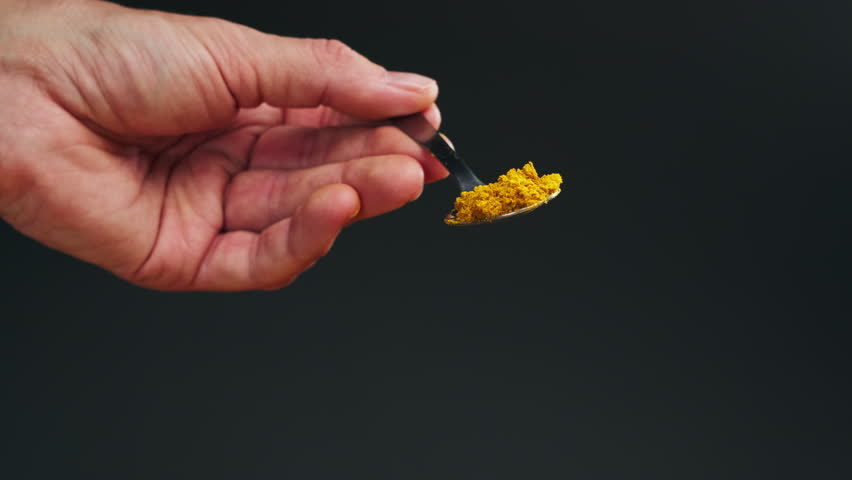 Spice turmeric powder on spoon close up. Sprinkle turmeric powder. Spice for food and drinks. Healthy