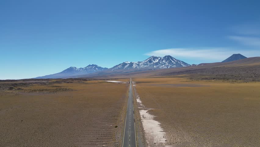 An aerial view of an unbroken desert road leading to the mountainous horizon in northern Chile