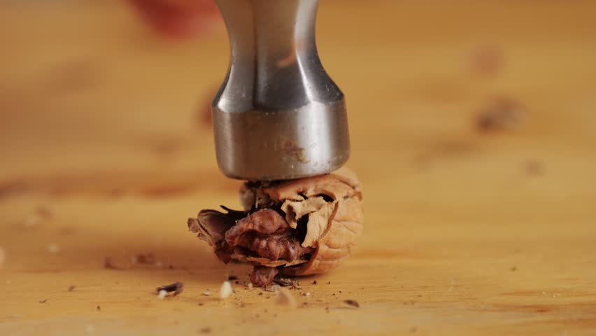 Craking walnut shell with hammer on wooden desk close-up. Healthy snacks. Product rich in minerals and vitamins.