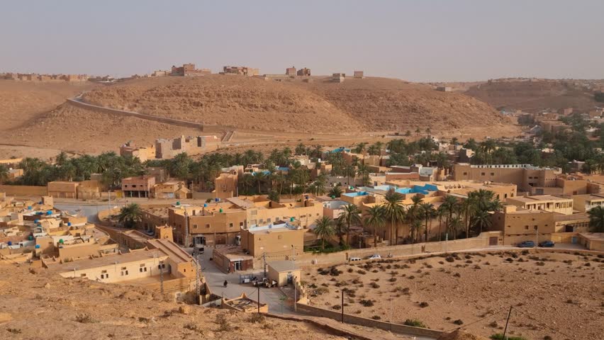 Panoramic view over Ghardaia’s outskirts in Algeria: traditional mud-brick homes, palm trees, and rolling desert hills reflect the charm of this Saharan oasis town