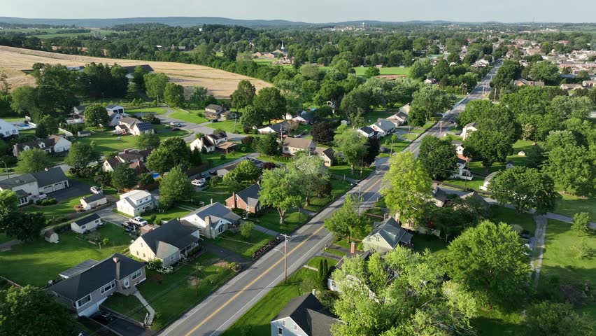 Serene Atmosphere in green neighborhood of American town. Golden sunset over quiet and quaint housing area. Single family homes in idyllic community. Aerial flyover.