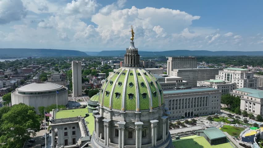 Aerial orbit of green cupola of Pennsylvania state capitol building in Harrisburg. Sunny day with clouds at sky. Historic buildings in American town.