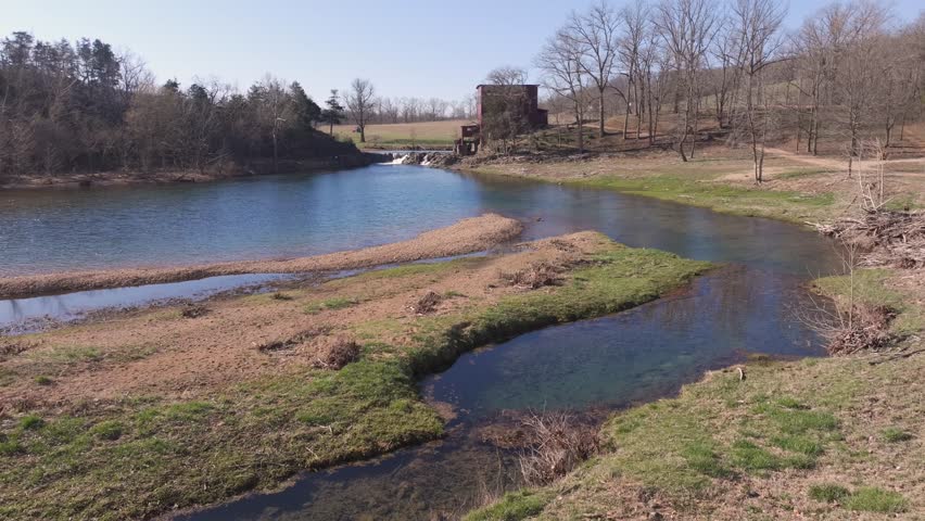 Aerial view of the rustic red mill standing proudly next to a gentle waterfall cascading into the clear waters, Burfordville, Missouri, United States.