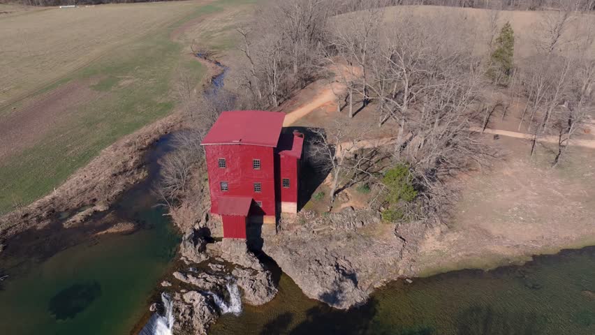Aerial view of the red mill building next to the water, framed by trees, creating a striking contrast against the natural landscape, Burfordville, Missouri, United States.