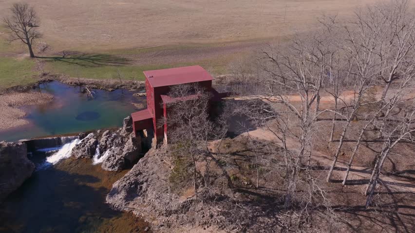 Aerial view of the vibrant red mill building standing proudly near a small waterfall, contrasting with the surrounding landscape, Burfordville, Missouri, United States.