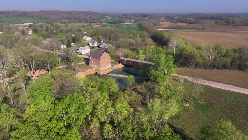 Aerial view of the historic Bollinger Mill and covered bridge surrounded by vibrant green trees and open fields, Burfordville, Missouri, United States.