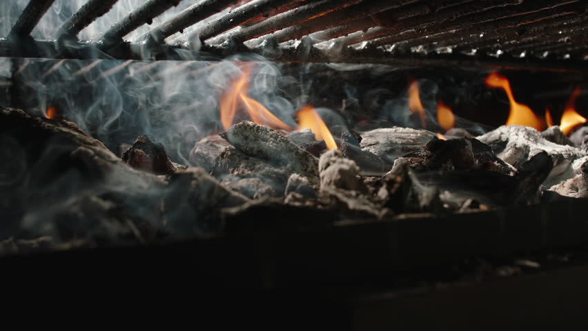 Juicy T-bone steak grilling on barbecue with flames and smoke, slow motion 4K