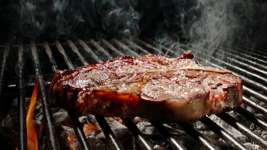 BBQ T-bone Steak Grilling over Open Fire with Flames and Smoke, 4K Slow Motion