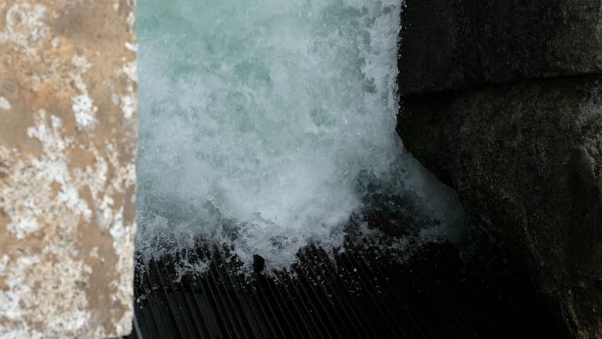 Mountain water overflows over a dam and quickly falls onto a metal grate. Catalan Pyrenees, Spain.